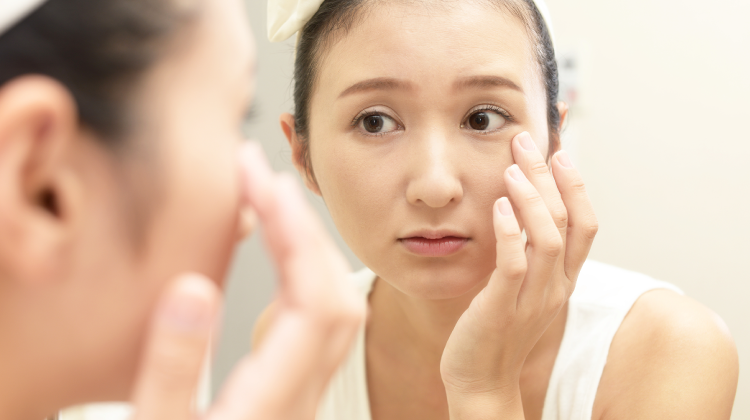 鏡でほうれい線を確認する女性 ─ フェイスラインのたるみ・むくみが気になるイメージ